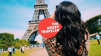 A woman traveler taking a photo of the Eiffle Tower in Paris, France.  The Adept Traveler Logo is centered in the middle of the picture.