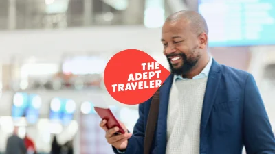 A man looks at his phone while traveling, the Adept Traveler logo overlays this image.