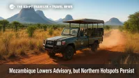 Safari truck navigates dusty Niassa Reserve track amid granite hills under bright sky, illustrating Mozambique travel advisory.