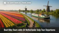 Cyclists ride beside brilliant tulip fields as a small barge cruises a canal near historic windmills, showcasing bike and barge Netherlands tulip tours in spring.