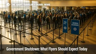 A busy TSA checkpoint shows longer lines as the government shutdown travel impact begins, with stanchions and lane signs visible under bright morning light.