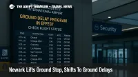 Newark Liberty departures board shows Ground Delay Program in effect, with wet reflections and security wayfinding during staffing-related delays