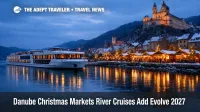 Danube Christmas markets river cruises, a modern river ship passes Vienna's lit waterfront beside winter market stalls.